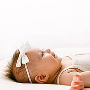 Ava participe au concours pour gagner de l'argent avec cette photo : arm, baby, baby_girl, bright_background, child, closeup, cute, face, hand, happy, headband, infant, lying_down, newborn, portrait, skin, smiling, soft_surface, white_bow, white_outfit