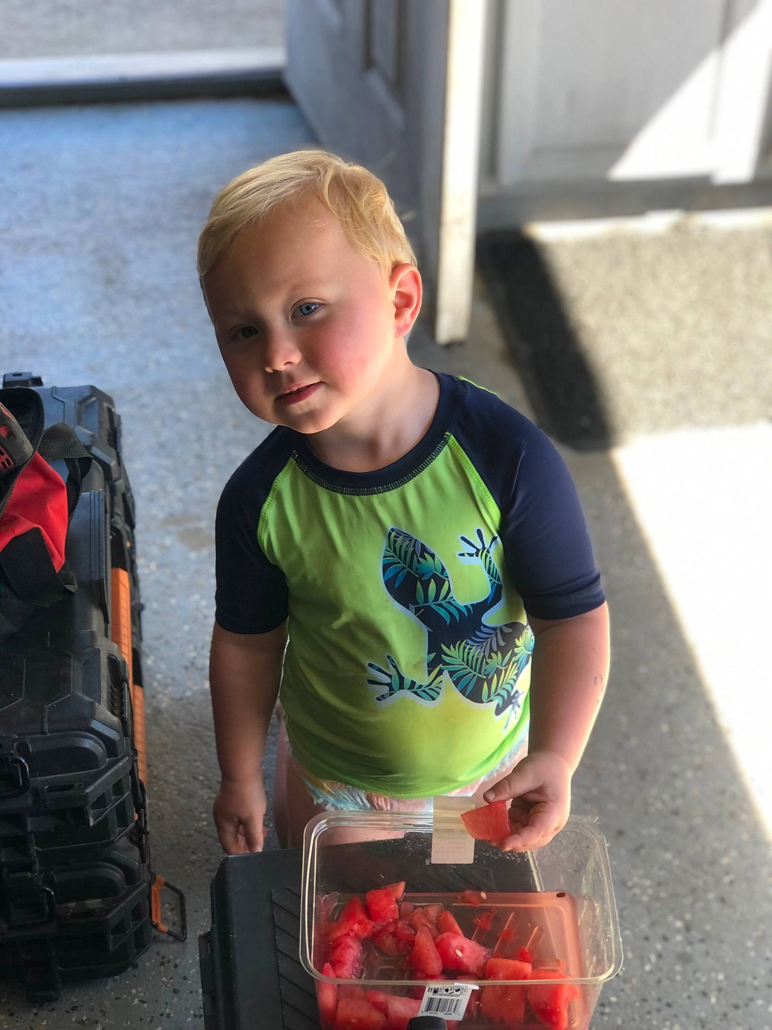 Lane is registered to the contest to win money with this photo: backpack, bag, baggage, carmine, child, fruit, fun, luggage_and_bags, person, personal_protective_equipment, recreation, red, service, shorts, sitting, t_shirt, toddler, toy, travel