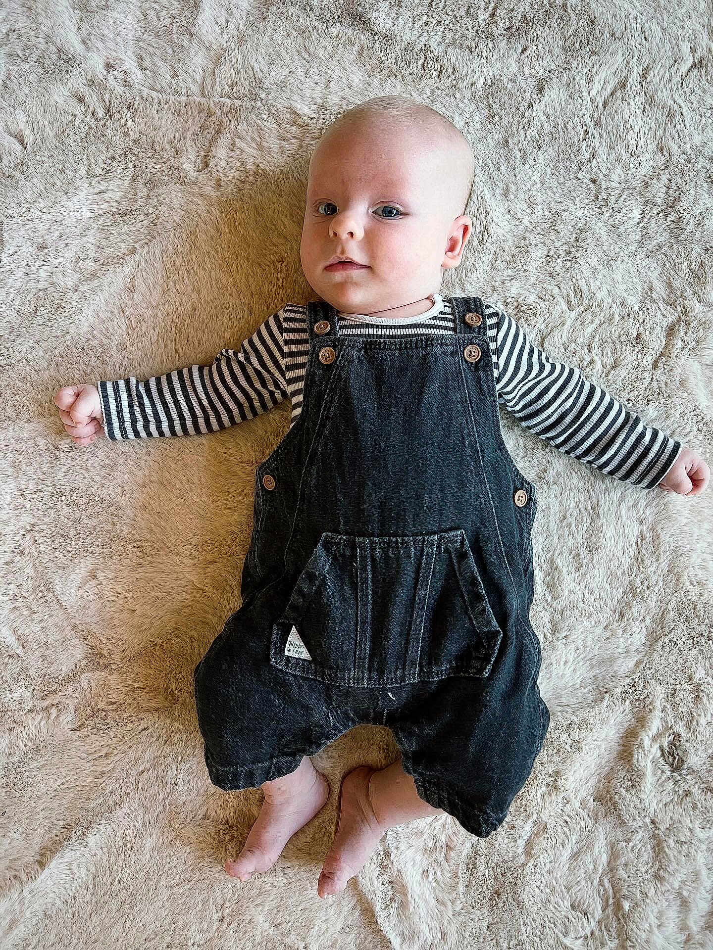 Beauden participe au concours pour gagner de l'argent avec cette photo : baby, infant, child, overalls, striped_shirt, barefoot, soft_rug, lying_down, curious_expression, indoor, cute, small_feet, button_details, denim, portrait, casual_clothing, relaxed_pose, neutral_expression, light_skin, closeup