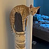 cat, ginger_cat, scratching_post, indoor, furniture, bedroom, bed, blanket, curious, pet, animal, orange, feline, domestic_cat, resting, wall, doorframe, floor, rope, cozy