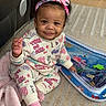 toddler, child, smiling, headband, colorful_clothing, pink_socks, blanket, water_mat, carpet, indoor, cute, happy, sitting, playful, floor, person, young_child, curly_hair, cozy, home