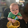 Richard joined the competition — help win amazing prizes! baby, child, high_chair, food, spoon, messy_face, blue_eyes, green_shirt, plate, yellow_plate, eating, mealtime, indoor, blurred_background, cute, person, infant, feeding, kitchen, toddler