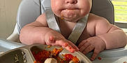Clinton is registered to the contest to win money with this photo: baby, high_chair, food, messy, plate, silicone_pacifier, indoor, window, blinds, expression, cheeks, arm, hand, skin, hair, child, meal, tongue, table, light