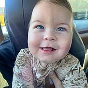 Clinton is registered to the contest to win money with this photo: baby, child, smile, blue_eyes, face, hand, clothing, animal_print, car_interior, seat, portrait, happy, cute, infant, person, apparel, light, young_child, skin, sitting