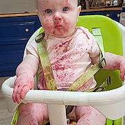 Briella is registered to the contest to win money with this photo: baby, high_chair, kitchen, messy, berry_stains, face, arms, legs, straps, clothing, expression, child, indoor, floor, cabinet, countertop, appliance, skin, foot, hand