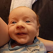 Gabriel is registered to the contest to win money with this photo: baby, smile, face, child, infant, person, clothing, striped, blue, gray, arm, towel, hair, skin, closeup, happy, indoors, portrait, fabric, button