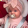 baby, infant, pacifier, headband, pink_clothing, car_seat, safety_strap, cute, child, portrait, indoors, seat, red_background, baby_girl, closeup, smiling, soft_texture, cozy, adorable, baby_accessory
