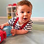 baby, child, toy, striped_shirt, indoor, playroom, floor_mat, curious, happy, infant, person, face, hand, crawling, cute, young, expression, soft_light, blurred_background, red_suspender