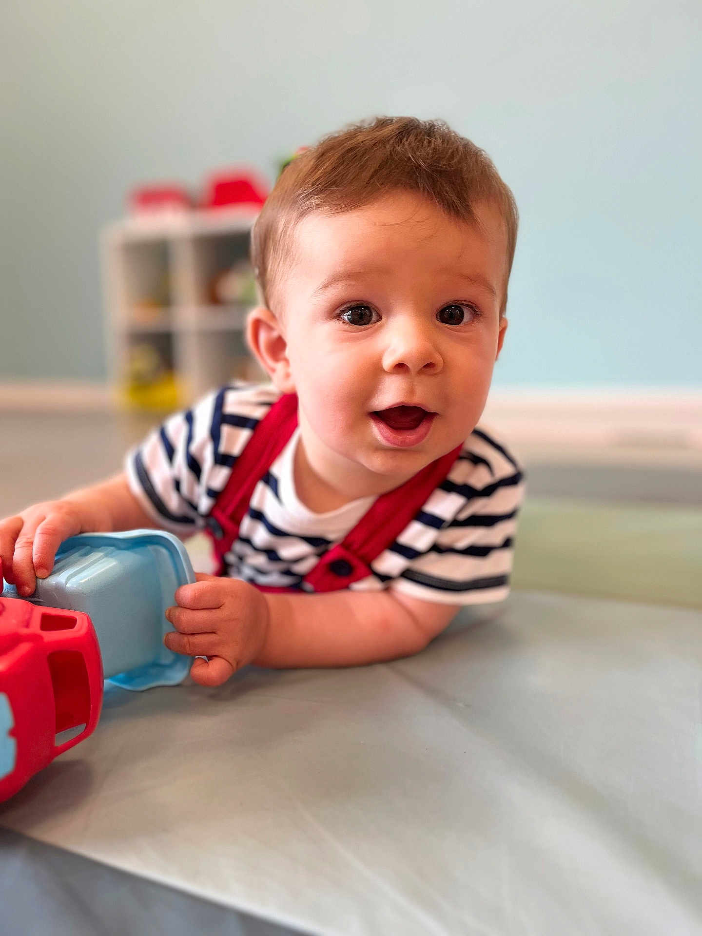Hugo participe au concours pour gagner de l'argent avec cette photo : baby, child, toy, striped_shirt, indoor, playroom, floor_mat, curious, happy, infant, person, face, hand, crawling, cute, young, expression, soft_light, blurred_background, red_suspender