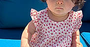 Stella joined the competition — help win amazing prizes! toddler, child, baby, curly_hair, blue_cushion, floral_dress, pink_socks, sitting, outdoor, sunlight, portrait, cute, innocent, expression, person, face, young_child, casual_clothing, relaxed, closeup
