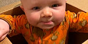 Bryson is registered to the contest to win money with this photo: baby, cardboard_box, carpet, child, childrenswear, curious, cute, face, floor, head, home, indoor, infant, monkey_print, onesie, orange_clothing, person, playful, sitting, young_child