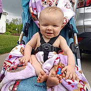 Bryson is registered to the contest to win money with this photo: baby, blanket, car, child, clothing, face, feet, grass, hand, happy, holding, outdoor, parking_lot, person, purple, sidewalk, smiling, stroller, toy, vehicle