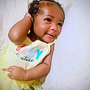 Treasure joined the competition — help win amazing prizes! baby, infant, smiling, lying_down, pillow, blanket, dress, yellow_dress, bow, hair, curly_hair, close_up, portrait, cute, hand, arm, bed, soft_lighting, eyes, happy