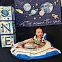 Joseph is registered to the contest to win money with this photo: baby, child, inflatable, spaceship, space, birthday, blocks, one, green_ball, smiling, indoor, decorations, celebration, happy, person, toy, costume, banner, planet, rocket