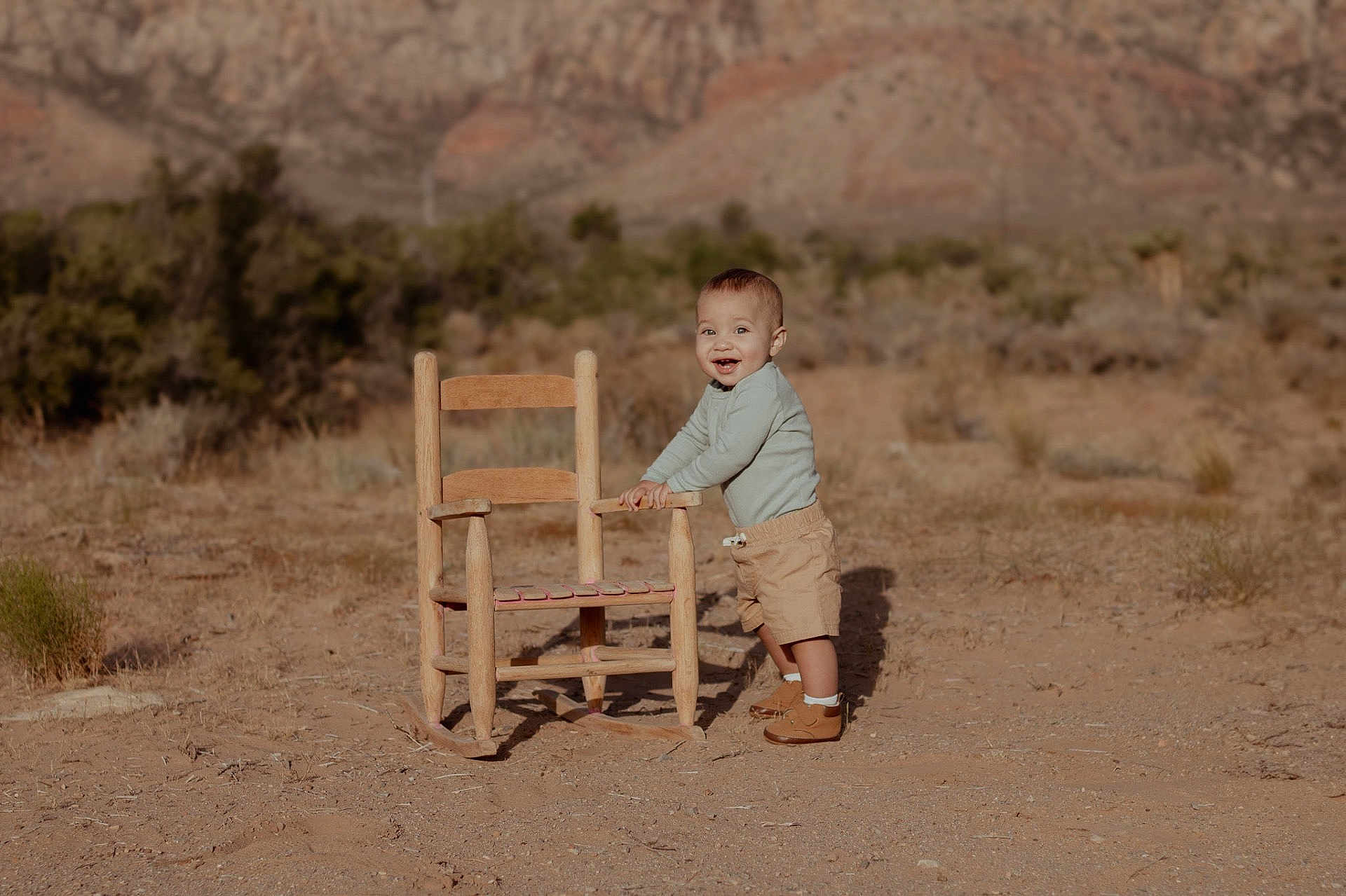 Joseph joined the competition — help win amazing prizes! toddler, child, outdoor, desert, rocking_chair, smiling, mountains, nature, dry_landscape, baby, standing, clothing, boots, shorts, long_sleeve, sunlight, happy, playing, toy, person