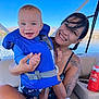 Joseph joined the competition — help win amazing prizes! baby, child, woman, life_jacket, boat, water, lake, mountains, smile, tattoo, outdoor, sunny, blue_sky, happy, holding, person, clothing, seat, vacation, summer