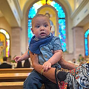 Joseph joined the competition — help win amazing prizes! baby, child, indoor, church, stained_glass, colorful, holding, person, portrait, curious, blue_clothing, scarf, hands, bench, religious, architecture, wristband, patterned_clothing, seated, people