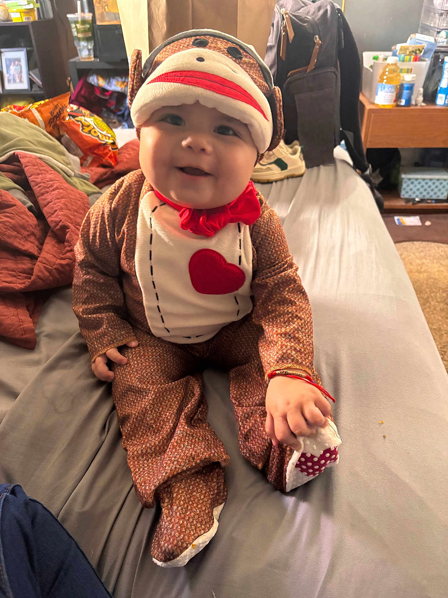Paxton is registered to the contest to win money with this photo: baby, bed, casual, child, clothing, costume, cute, fabric, face, footwear, hand, happy, home, indoor, person, plush, red_bow, smiling, sock_monkey, toy