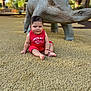 baby, child, cute, daylight, dinosaur_sculpture, fun, grass, happy, infant, nature, outdoor, park, person, playground, red_clothing, sculpture, sitting, smile, summer, toy