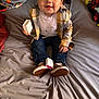 Paxton is registered to the contest to win money with this photo: toddler, child, smiling, indoor, plaid_jacket, jeans, sneakers, necklace, bed, blanket, remote_control, toy, box, happy, cute, person, clothing, sitting, face, portrait