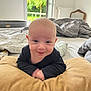 baby, infant, pillow, bed, blanket, smile, face, indoors, window, greenery, clothing, person, head, happy, furniture, room, light, skin, young_child, expression