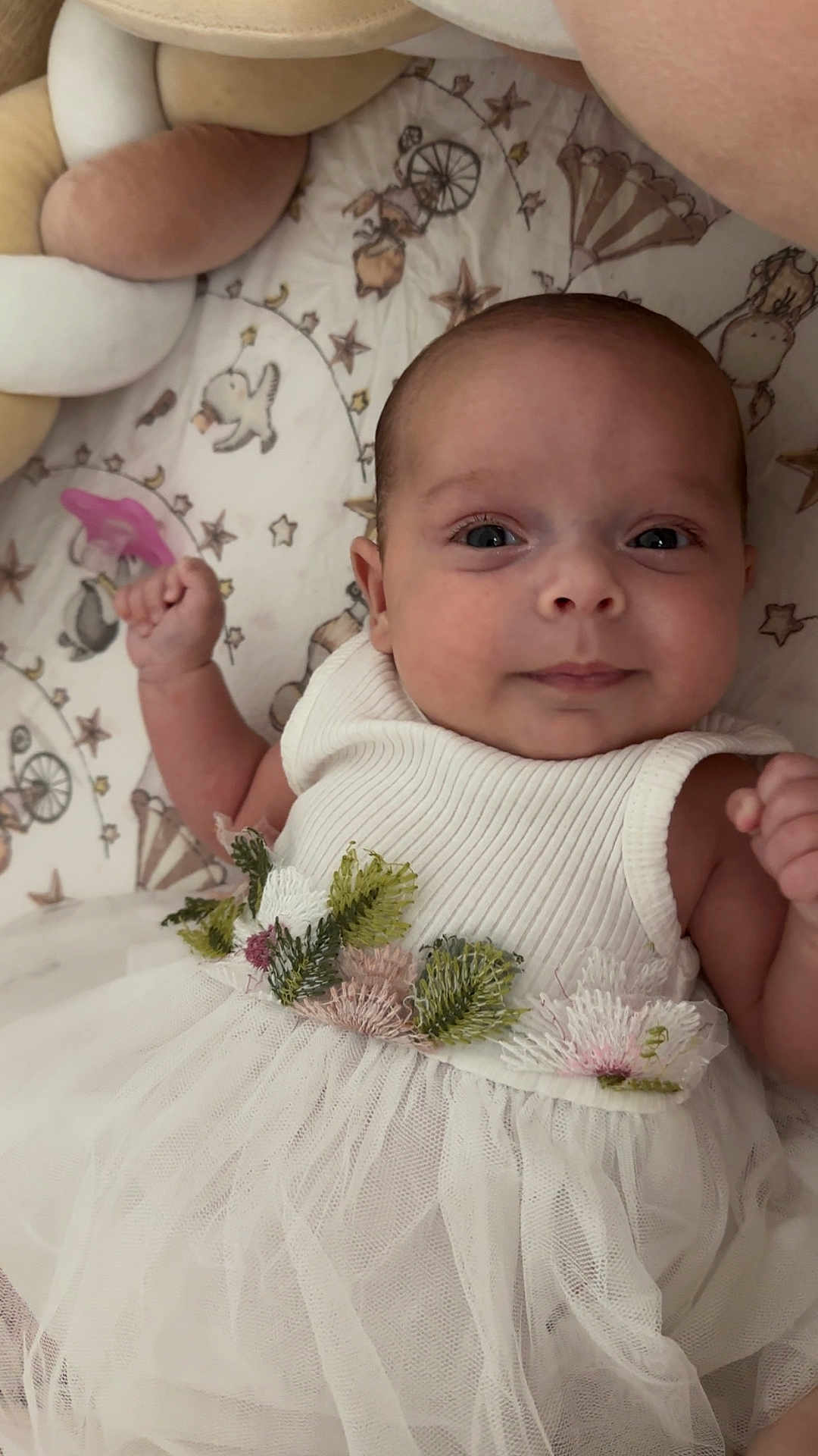 Maria participe au concours pour gagner de l'argent avec cette photo : baby, infant, dress, white_dress, floral_embroidery, blanket, patterned_blanket, braided_cushion, fist, face, eyes, smile, skin, cute, lying_down, indoors, soft_lighting, portrait, newborn, child