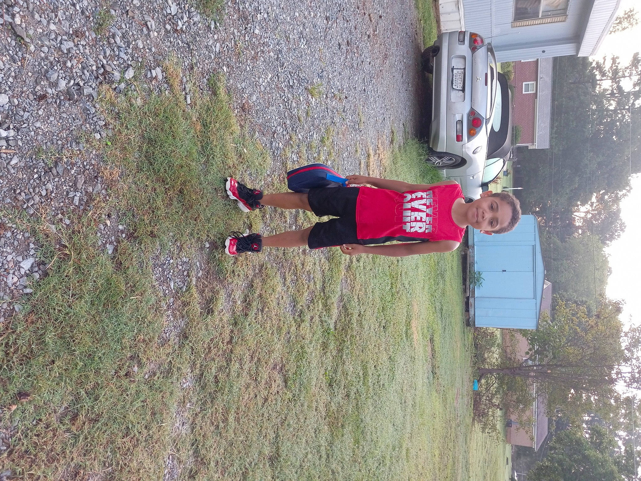 Denzel is registered to the contest to win money with this photo: adventure, automotive_exterior, car, carmine, family_car, fun, grass, joy, landscape, person, plant, recreation, shorts, sky, soil, sports_uniform, tire, tree, vehicle, walking_shoe