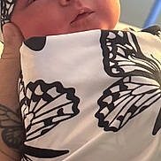Laycii is registered to the contest to win money with this photo: baby, infant, newborn, wrapped, blanket, headwrap, black_and_white, butterfly_pattern, tattoo, hand, close_up, soft_lighting, face, calm, cozy, indoor, person, skin, newborn_baby, portrait