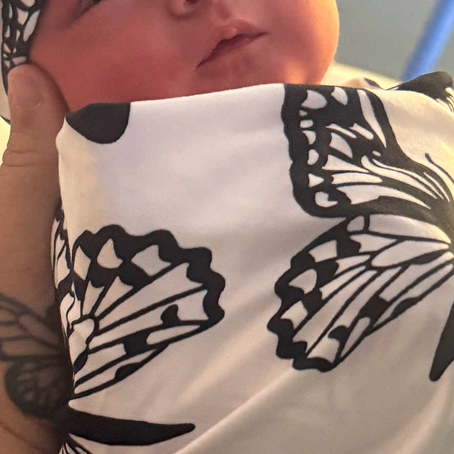 Laycii is registered to the contest to win money with this photo: baby, black_and_white, blanket, butterfly_pattern, calm, close_up, cozy, face, hand, headwrap, indoor, infant, newborn, newborn_baby, person, portrait, skin, soft_lighting, tattoo, wrapped