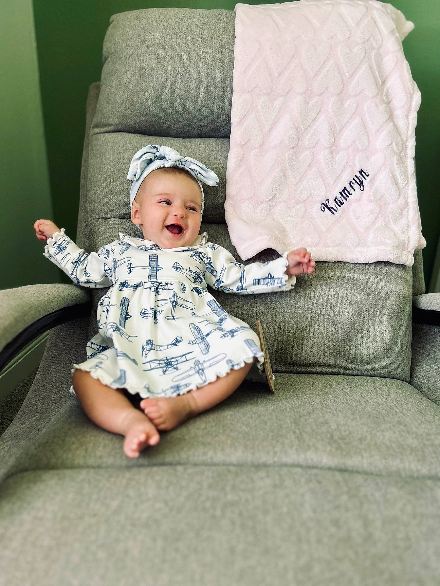 Kamryn is registered to the contest to win money with this photo: baby, baby_toddler_clothing, bedding, child, comfort, couch, flooring, foot, home_accessories, linens, pattern, person, pillow, portrait_photography, rectangle, room, sitting, sleeve, smile, throw_pillow