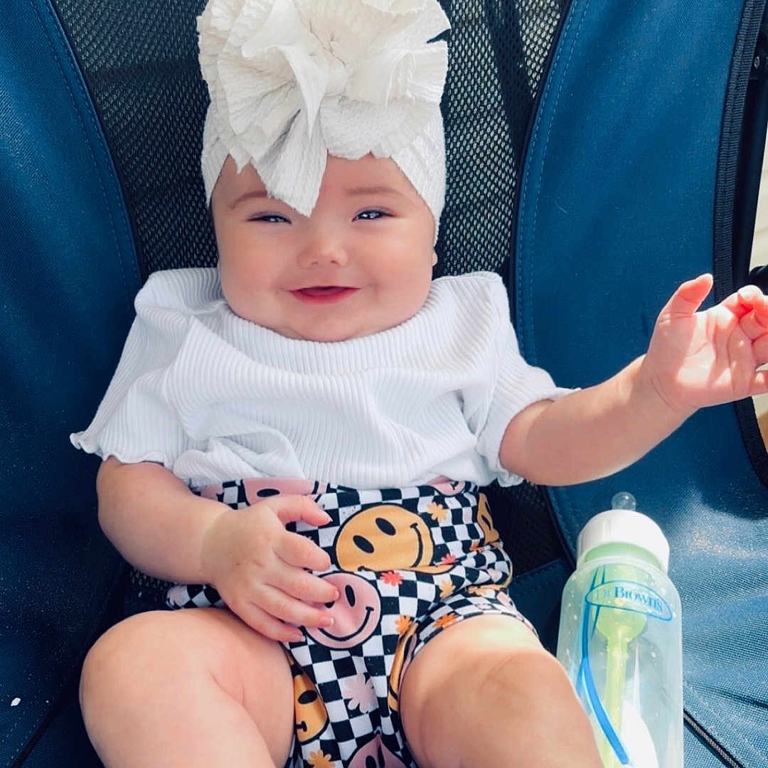 Scottlynn is registered to the contest to win money with this photo: baby, child, smile, white_top, headwrap, paper_towel, checkered_shorts, smiley_faces, baby_shoes, socks, blue_chair, baby_bottle, milk, happy, sitting, infant, cute, indoors, portrait, person
