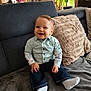 baby, child, smiling, indoor, couch, pillow, clothing, jeans, shirt, socks, furniture, happy, face, person, home, living_room, toddler, cute, seated, cozy