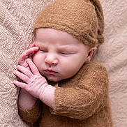 Malo participe au concours pour gagner de l'argent avec cette photo : baby, sleeping, infant, knitted_hat, knitted_outfit, cozy, peaceful, resting, hands, face, blanket, beige, brown, soft_texture, portrait, cute, newborn, child, closeup, toddler