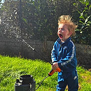 Noam Sohier a rejoint le concours — aidez-le/la à gagner de superbes lots ! blue_tracksuit, child, daylight, expression, fun, garden, grass, greenery, hair, hedge, nature, outdoor, person, play, sprayer, sunny, surprise, toy, water, white_shoes