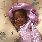 Nadirah is registered to the contest to win money with this photo: baby, sleeping, smiling, onesie, purple_clothing, blanket, cushion, unicorn_pattern, infant, cozy, cute, child, face, resting, bed, soft_fabric, happy, indoors, person, comfort