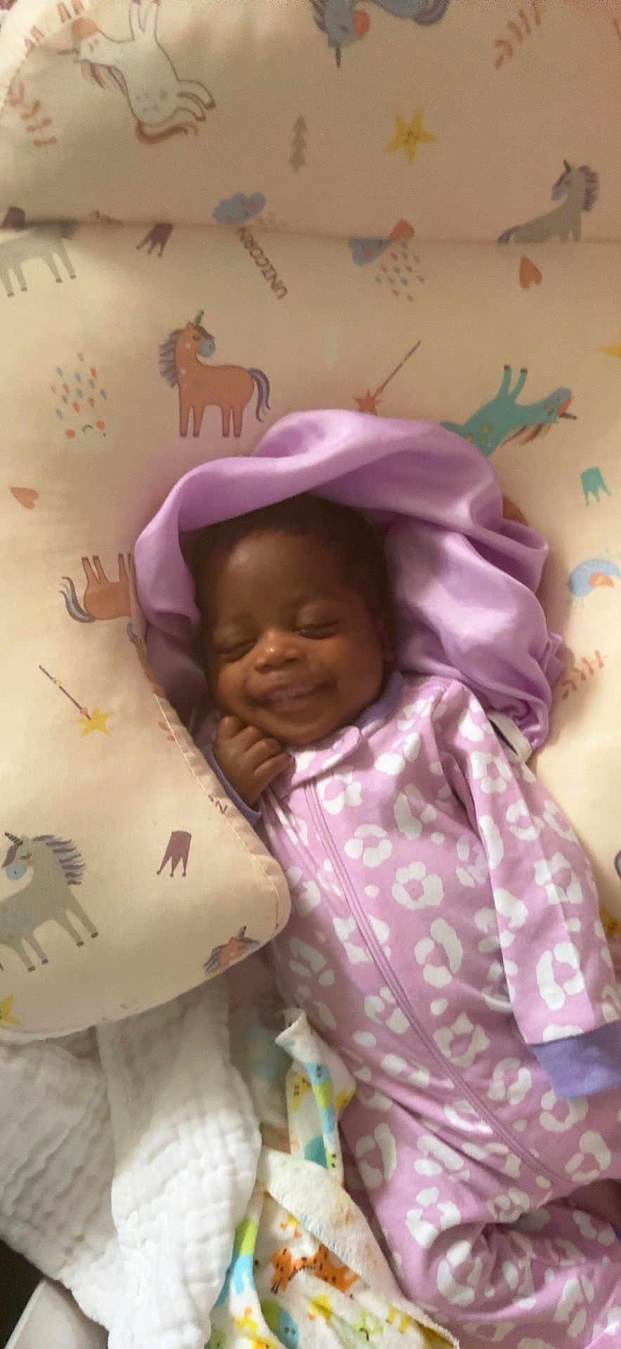 Nadirah is registered to the contest to win money with this photo: baby, sleeping, smiling, onesie, purple_clothing, blanket, cushion, unicorn_pattern, infant, cozy, cute, child, face, resting, bed, soft_fabric, happy, indoors, person, comfort