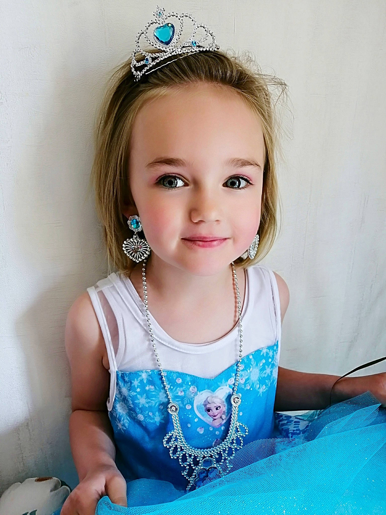 Elana a rejoint le concours — aidez-le/la à gagner de superbes lots ! blond, blue, child, child_model, clothing, crown, dress, face, fashion_accessory, hair, hair_accessory, head, headband, headgear, headpiece, jewellery, person, smile, tiara, toddler