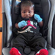 Travis is registered to the contest to win money with this photo: baby, infant, car_seat, clothing, mittens, black_clothes, red_booties, knitted_booties, baby_jogger, seat_belt, person, portrait, indoor, child, cute, young, face, head, sitting, expression