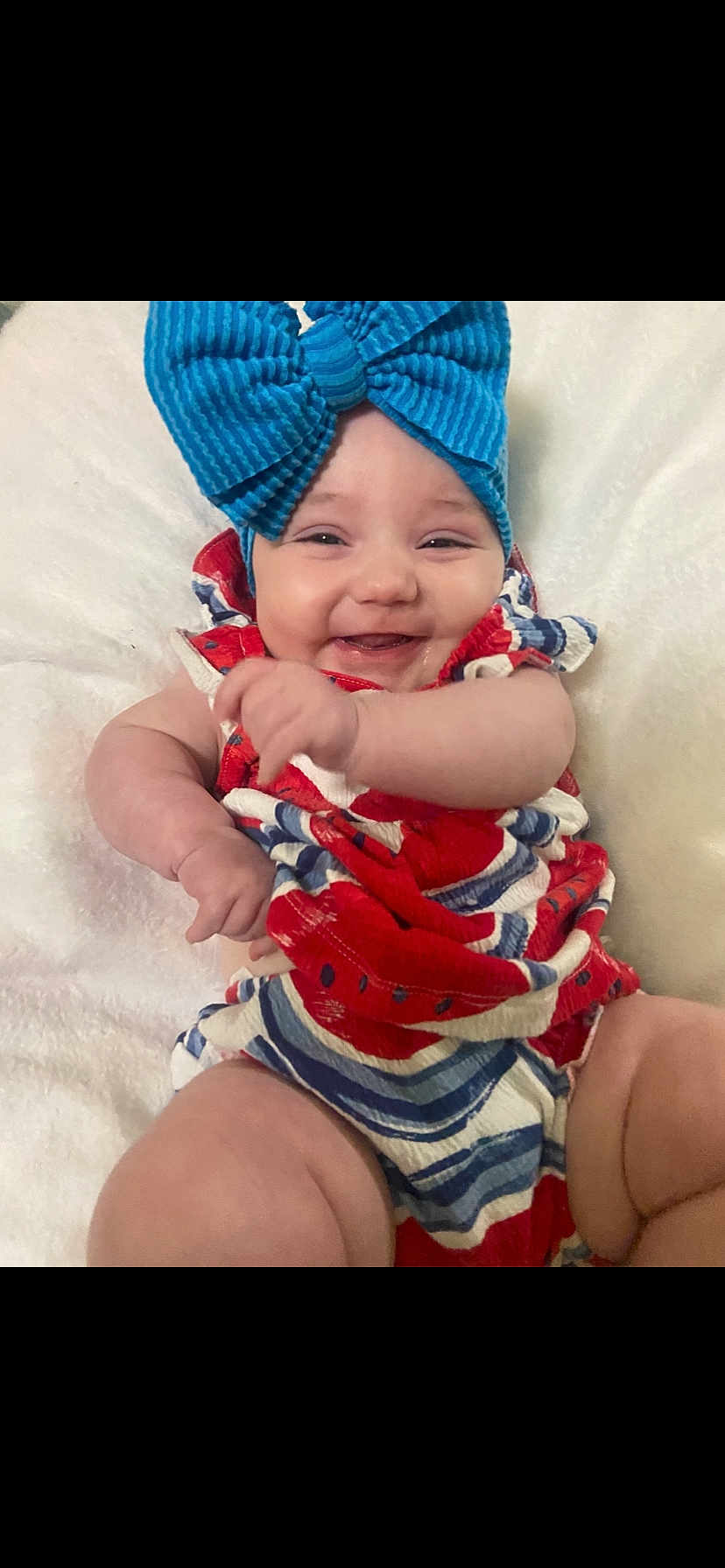 Blakelee is registered to the contest to win money with this photo: baby, smiling, blue_bow, red_clothing, white_blanket, happy, infant, child, cute, portrait, close_up, chubby_arms, candid, indoors, soft_texture, colorful_outfit, cheerful, person, headwear, playful