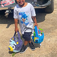 Jakobi joined the competition — help win amazing prizes! child, boy, easter_basket, plush, braided_hair, tshirt, shorts, sneakers, sunlight, outdoor, driveway, vehicle, license_plate, concrete, smiling, holding, toy, holiday, spring, daytime