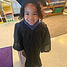 Jakobi is registered to the contest to win money with this photo: child, graduation_gown, graduation_cap, smiling, indoor, classroom, toy_shelf, paper_bag, curly_hair, happy, floor_tiles, purple_rug, educational_setting, young_child, portrait, person, celebration, preschool, kindergarten, school