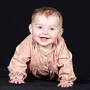 Lio participe au concours pour gagner de l'argent avec cette photo : baby, child, smiling, crawling, blue_eyes, peach_outfit, long_sleeves, happy, cute, portrait, indoor, infant, young_child, face, hands, studio_photo, black_background, clothing, person, small_fingers