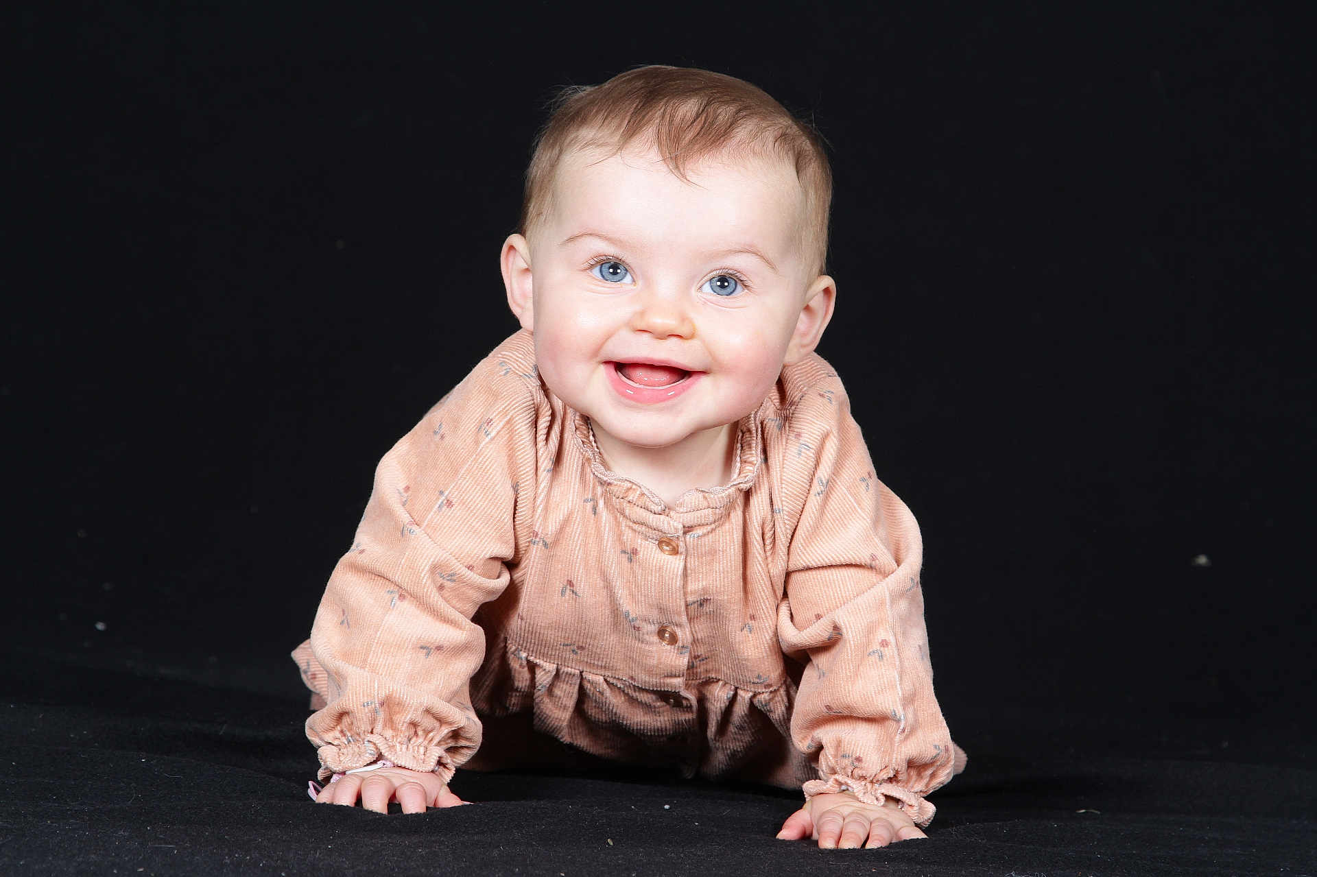 Lio participe au concours pour gagner de l'argent avec cette photo : baby, child, smiling, crawling, blue_eyes, peach_outfit, long_sleeves, happy, cute, portrait, indoor, infant, young_child, face, hands, studio_photo, black_background, clothing, person, small_fingers