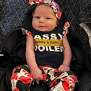 Khalilah joined the competition — help win amazing prizes! baby, infant, car_seat, headband, bow, onesie, graphic_tee, floral_pants, patterned_clothing, smile, face, hands, arms, legs, socks, quilted_blanket, seat_buckle, black_background, red_white_black, portrait