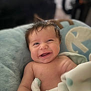 Rhyland is registered to the contest to win money with this photo: baby, smiling, laughing, blanket, cushion, soft_fabric, wet_hair, indoors, child, happy, cute, portrait, infant, skin, person, cozy, comfort, head, face, expression