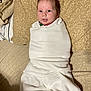 baby, infant, blanket, white_clothing, bed, pillow, patterned_bedspread, face, eyes, smile, wrapped, cozy, indoors, child, newborn, cute, soft_texture, lying_down, portrait, home