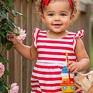 Camila joined the competition — help win amazing prizes! toddler, child, red_bow, striped_dress, toy_boat, golden_retriever, dog, roses, flowers, wooden_deck, outdoor, greenery, smiling, curly_hair, baby, summer, playful, cute, portrait, nature