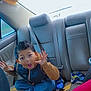 backseat, barefoot, blue_pants, car_interior, car_seat, casual_clothing, child, excited, expression, funny_face, hands_up, indoors, jacket, messy_seat, playful, seat_cushion, seatbelt, shoes, window, young_boy
