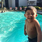 Matheyo is registered to the contest to win money with this photo: child, boy, smiling, pool, water, swimming, outdoor, sunlight, summer, building, chairs, happy, splash, fun, vacation, leisure, person, swimwear, blue, daylight
