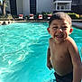 child, boy, smiling, pool, water, swimming, outdoor, sunlight, summer, building, chairs, happy, splash, fun, vacation, leisure, person, swimwear, blue, daylight